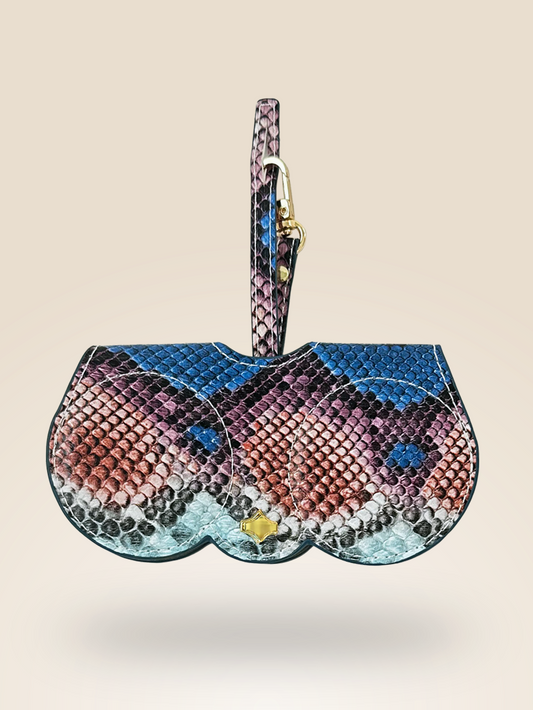 A stylish eyewear case charm in a bold python-inspired pattern featuring shades of blue, pink, and black. Made from vegan leather, it has a gold-tone clasp and a matching strap for easy attachment to bags. Designed for a chic and functional accessory.