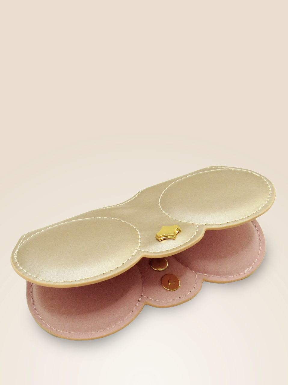 Open view of a champagne-colored vegan leather eyewear case charm, showcasing its dual compartments lined with soft pink fabric. The case features a secure magnetic snap closure with a small, gold-tone star detail on the front, accentuated by stitching along the edges.